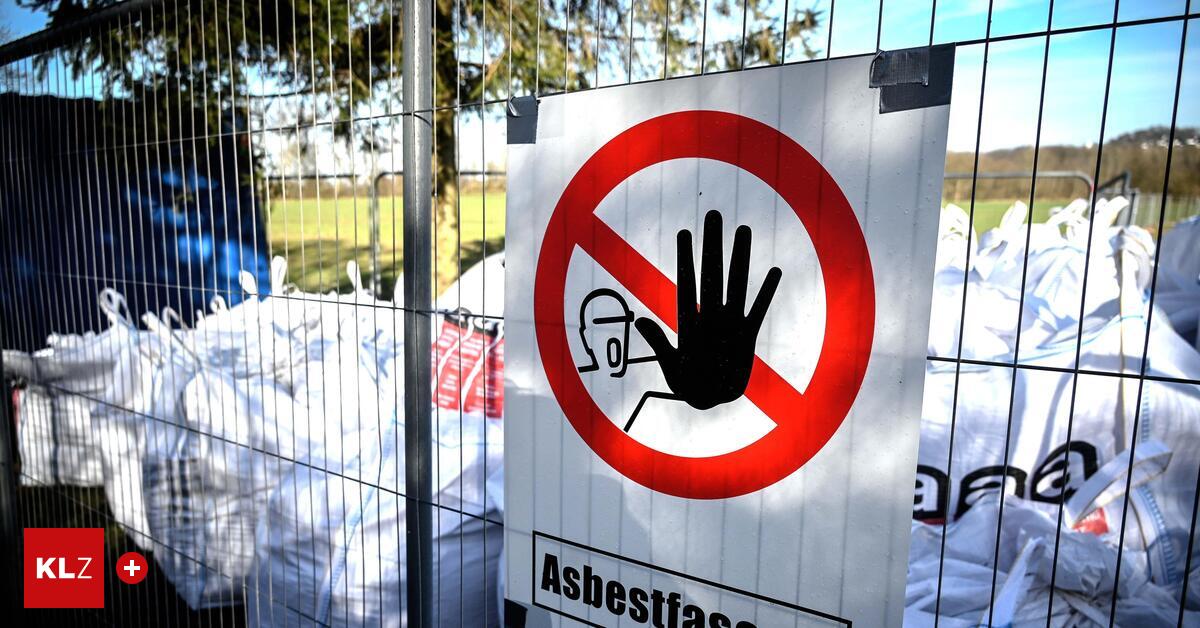 Warnschild auf einem Zaun mit dem Hinweis (Asbestfasern). Dahinter liegen etliche weiße Säcke